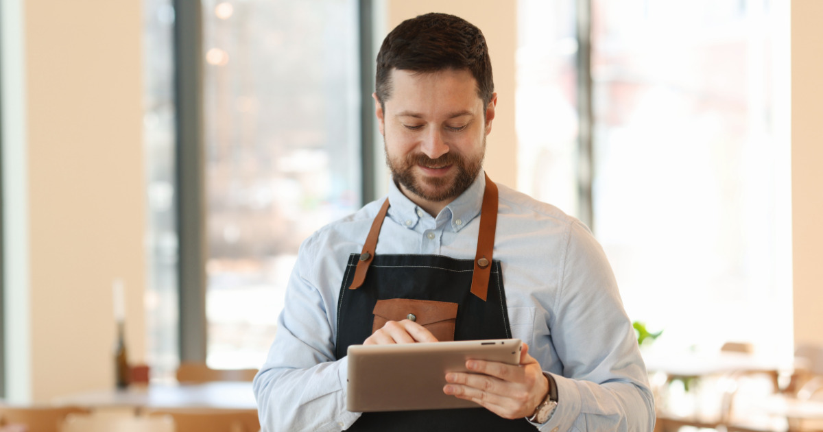A restaurant owner smiles at his tablet as he reviews Dine Local orders. The words Taking Back Control: Why Dine Local is the Smartest Choice for Your Ontario Restaurant are overlayed.