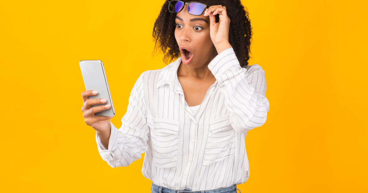 A surprised woman lifting her glasses in shock while looking at her phone, reacting to marked-up menu prices on a third-party delivery app