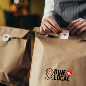 Image of an independent restaurant owner holding takeout bags with the Dine Local logo on them.